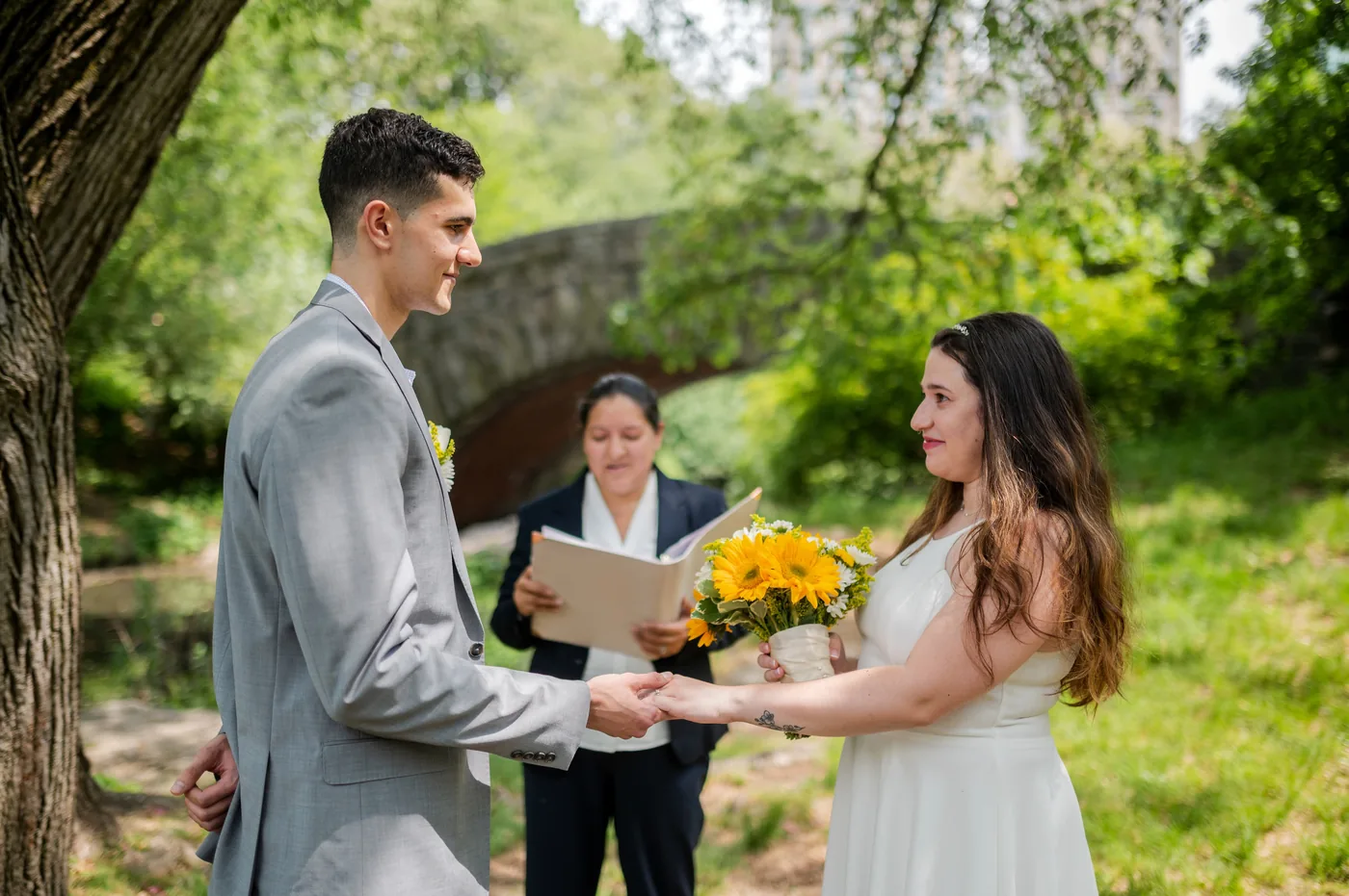 Pareja intercambiando votos en boda civil en Central Park con oficinante de Bodas NYC bajo puente de piedra