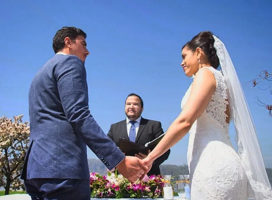 Pareja tomándose de las manos durante ceremonia de boda civil exterior en Nueva York con oficinante bilingüe
